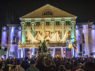 Das Deutsche Nationaltheater Weimar erstrahlt in bunten Lichtern, während eine Menschenmenge eine Veranstaltung im Freien genießt.