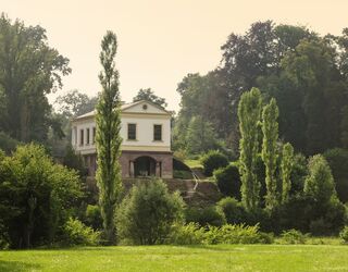 Roemisches Haus im Park an der Ilm Ein historisches Gebäude thront auf einer kleinen Anhöhe, umgeben von einer üppigen, grünen Landschaft und sanften Hügeln.